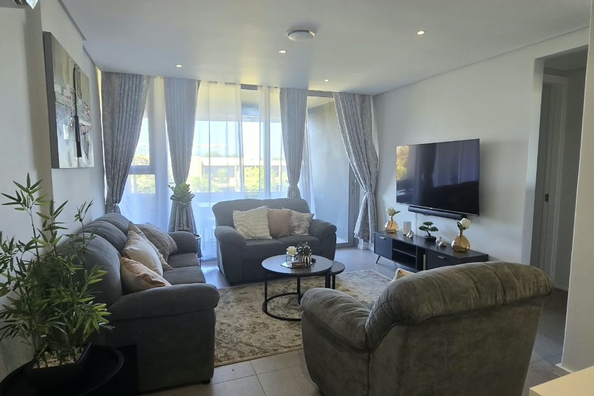 A well-maintained living room featuring tiled flooring, recessed downlighting, and direct access to a balcony through sliding glass doors.