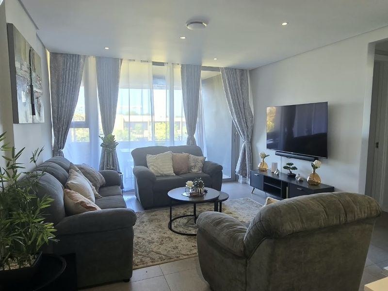A well-maintained living room featuring tiled flooring, recessed downlighting, and direct access to a balcony through sliding glass doors.