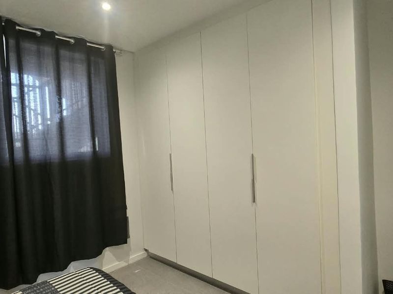 A well-maintained bedroom featuring floor-to-ceiling built-in cupboards, recessed downlighting, and a modern horizontal panel door.