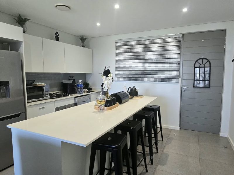 Modern kitchen featuring a central island with quartz countertops, sleek white cabinetry, recessed lighting, and tiled flooring.