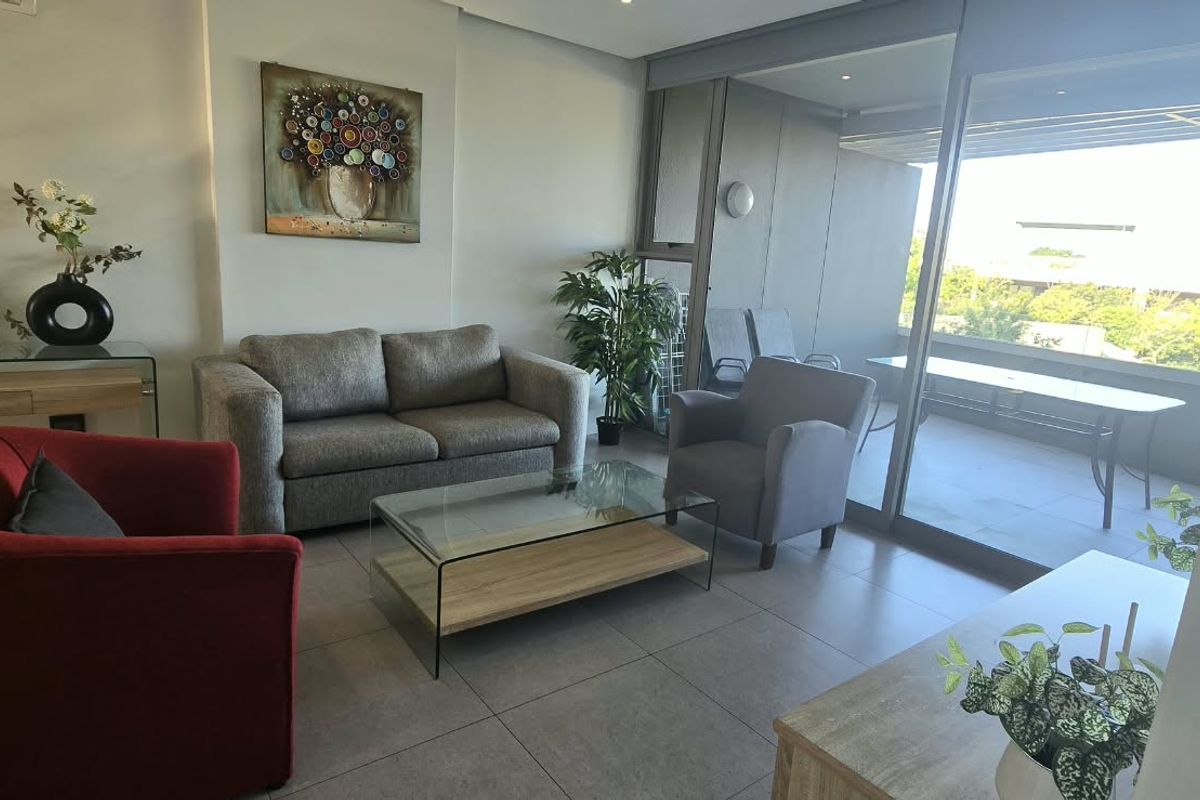 A bright and modern living room featuring large sliding glass doors that open onto a private balcony, complemented by neutral tiled flooring.