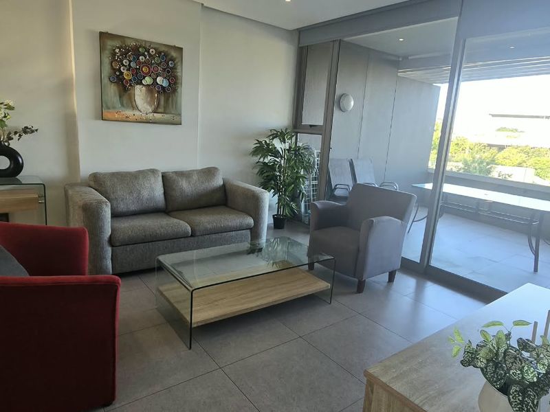 A bright and modern living room featuring large sliding glass doors that open onto a private balcony, complemented by neutral tiled flooring.