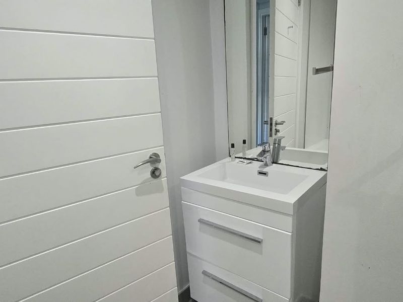 A modern bathroom featuring a white vanity cabinet with a basin, mixer tap, and a wall-mounted mirror.