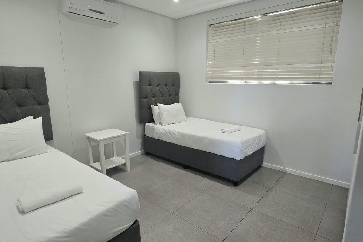A clean and modern bedroom featuring tiled flooring, an integrated air conditioning unit, and venetian blinds for privacy.