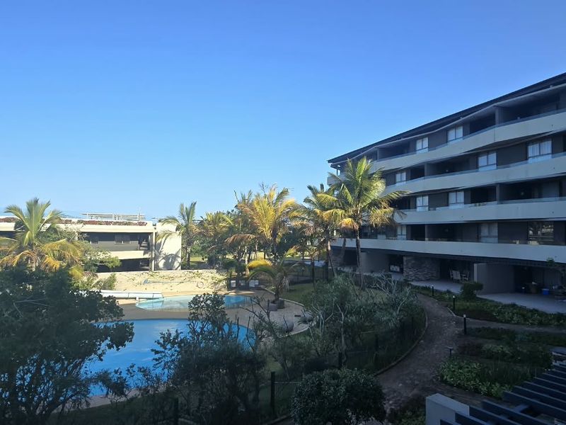 An elevated view of a modern apartment complex featuring a swimming pool, water slide, and well-maintained landscaped gardens.