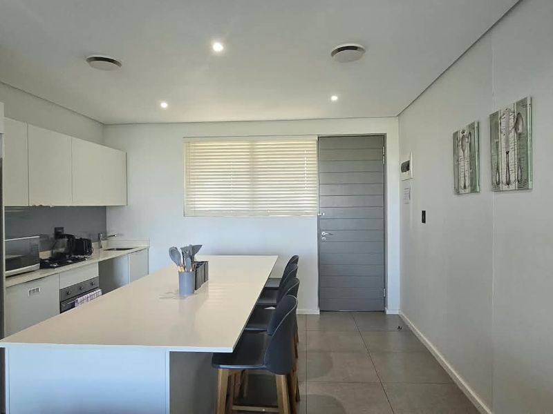 Modern open-plan kitchen featuring sleek cabinetry, stone countertops, integrated appliances, and recessed lighting, seamlessly flowing into the living area with tiled flooring.