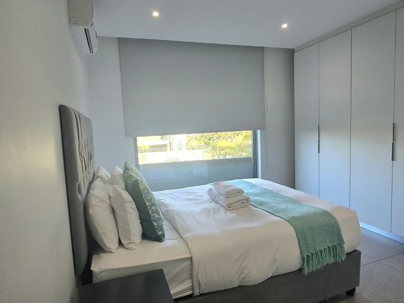 Modern bedroom featuring neutral tiled flooring, extensive built-in floor-to-ceiling cupboards, recessed lighting, and a wall-mounted air conditioning unit.