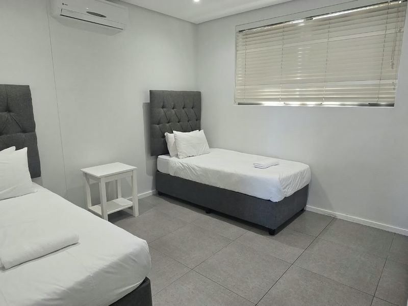 A clean and modern bedroom featuring tiled flooring, an integrated air conditioning unit, and venetian blinds for privacy.