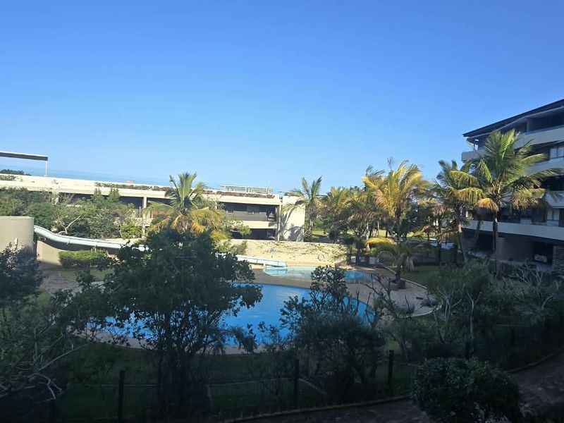 An elevated view of a communal swimming pool area with a water slide, surrounded by landscaped gardens and modern apartment blocks.