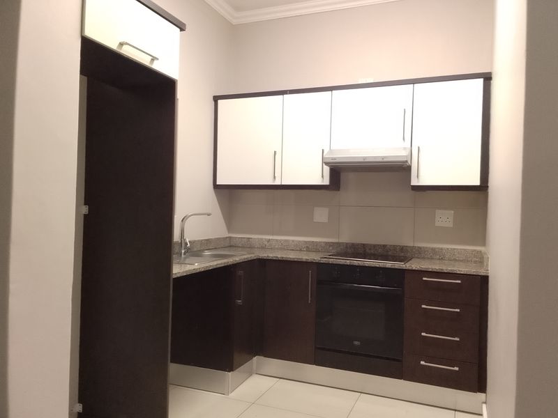 Modern kitchen featuring dark and white cabinetry, granite countertops, built-in oven, hob, extractor fan, and stainless steel sink with tiled flooring.
