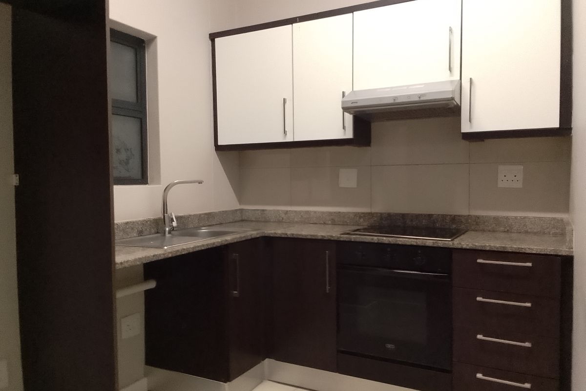 Modern kitchen featuring dark and white cabinetry, granite countertops, integrated oven, hob, and extractor fan with a clean tiled backsplash.