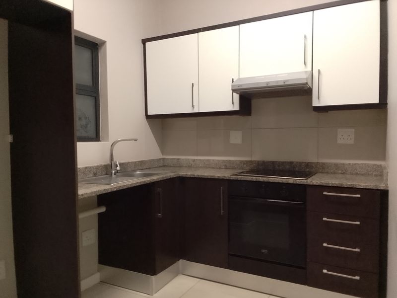 Modern kitchen featuring dark and white cabinetry, granite countertops, integrated oven, hob, and extractor fan with a clean tiled backsplash.