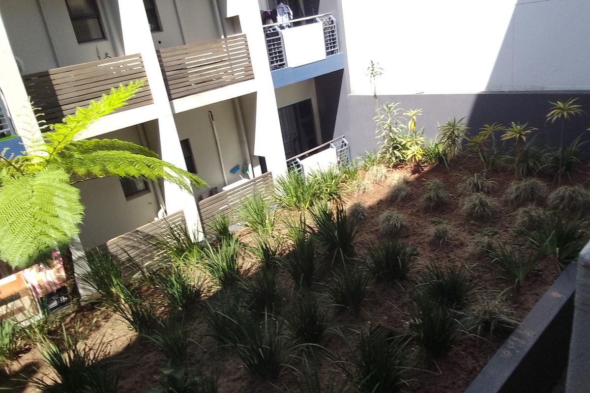An elevated view of a communal garden area featuring landscaped planting beds, surrounded by apartment building balconies with modern railings.