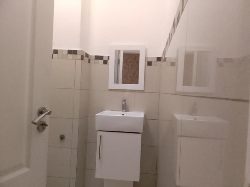 A compact, modern bathroom featuring a wall-mounted vanity unit, ceramic basin, chrome mixer tap, and neutral wall tiling with a decorative mosaic border.