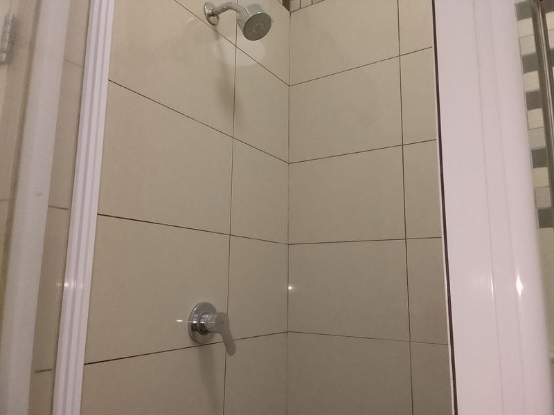 A functional shower enclosure featuring neutral wall tiles, a chrome shower mixer, and a fixed shower head.