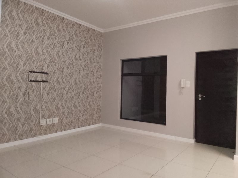 A bright, empty living room featuring neutral tiled flooring, a decorative textured feature wall, and an integrated intercom system.