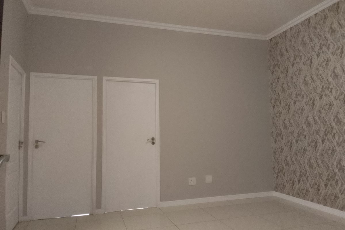 A clean, empty bedroom featuring neutral tiled flooring, a decorative patterned wallpaper accent wall, and crisp white interior doors.