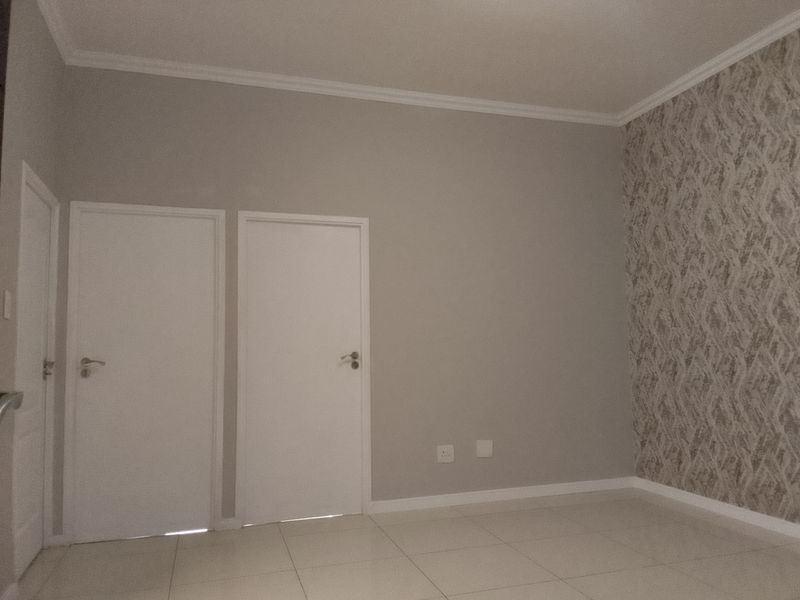 A clean, empty bedroom featuring neutral tiled flooring, a decorative patterned wallpaper accent wall, and crisp white interior doors.