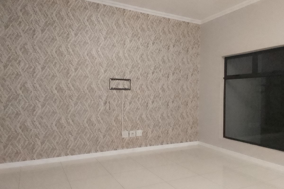 An empty living room featuring neutral tiled flooring, a decorative textured feature wall, and a wall-mounted TV bracket.