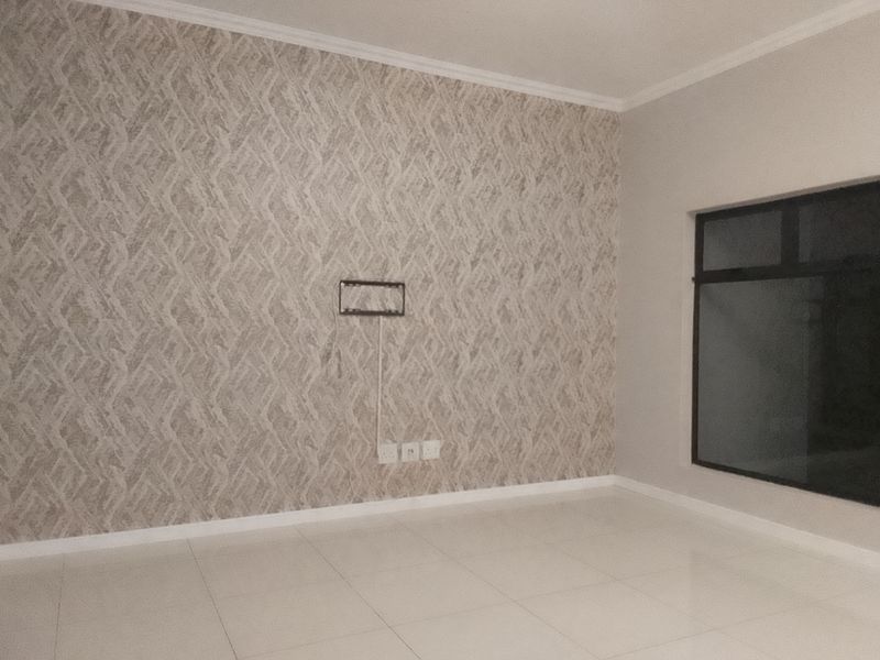An empty living room featuring neutral tiled flooring, a decorative textured feature wall, and a wall-mounted TV bracket.
