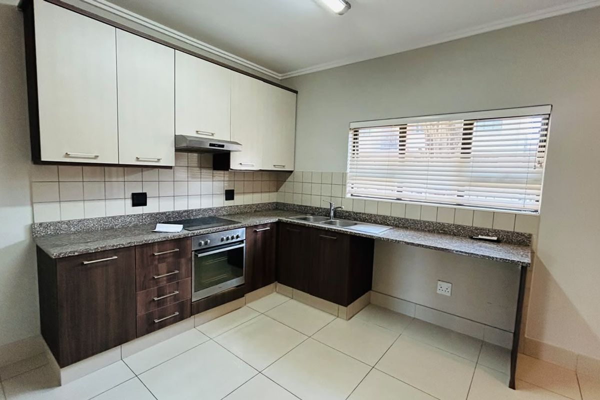 Modern kitchen featuring granite countertops, built-in oven, electric hob, extractor fan, double sink, and ample storage cabinetry with tiled flooring.