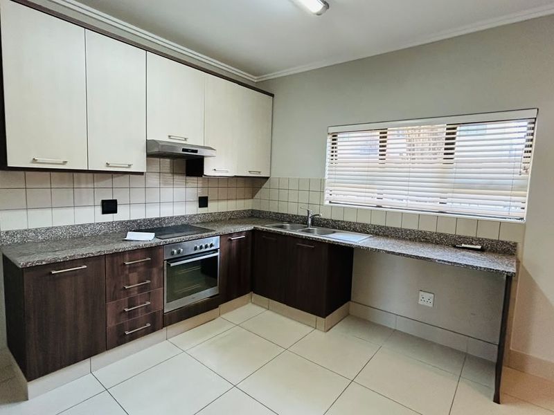 Modern kitchen featuring granite countertops, built-in oven, electric hob, extractor fan, double sink, and ample storage cabinetry with tiled flooring.