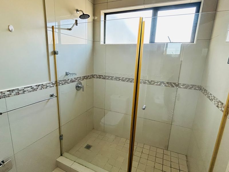 A clean, modern bathroom shower featuring a glass enclosure, mosaic tile accents, and neutral wall tiling.