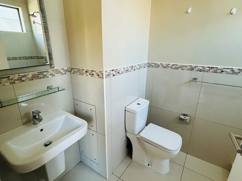A clean and well-maintained bathroom featuring a pedestal basin, toilet, and neutral tiled walls with a decorative mosaic border.