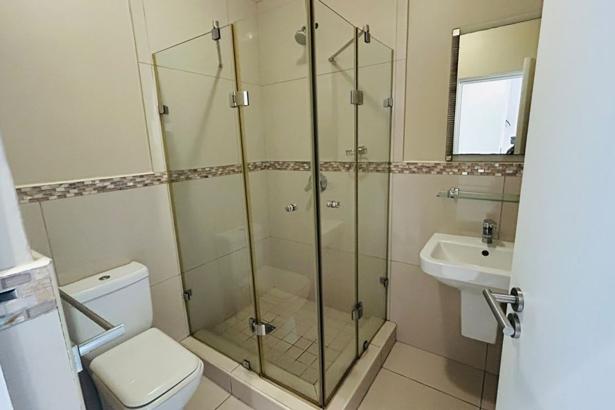A clean, functional bathroom featuring a glass-enclosed shower, pedestal basin, and toilet with neutral wall and floor tiling.
