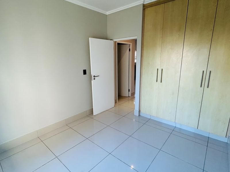 A clean, empty bedroom featuring neutral tiled flooring and ample built-in cupboard storage space.
