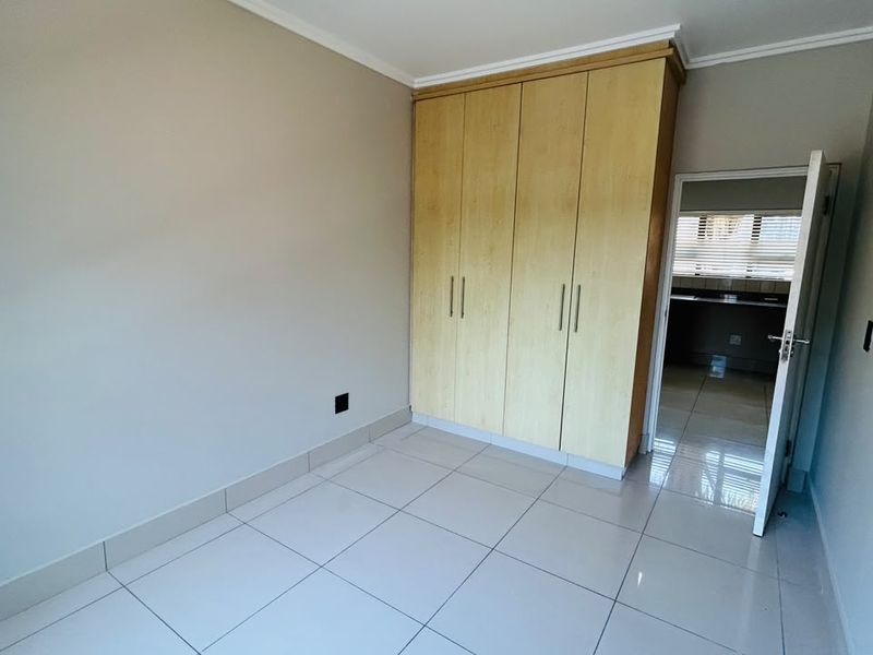 A clean, empty bedroom featuring neutral tiled flooring, built-in wooden cupboards, and a doorway leading to an adjacent room.