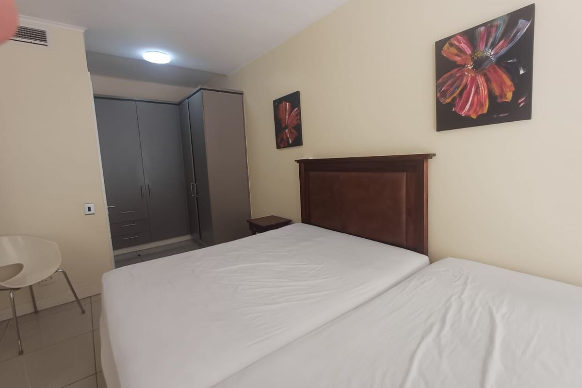 A functional bedroom featuring built-in cupboards, tiled flooring, and neutral wall finishes, providing a clean and practical living space.
