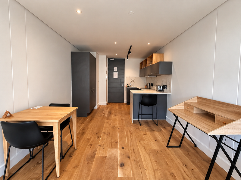 A modern open-plan apartment living space featuring high-quality hardwood flooring, contemporary cabinetry, and a functional kitchen island with integrated storage.