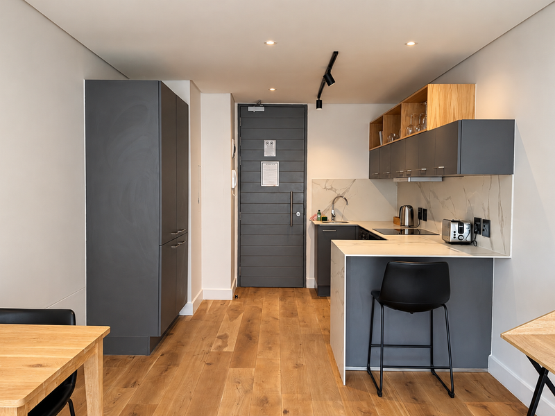 Modern open-plan kitchen featuring sleek grey cabinetry, stone countertops, marble-look splashback, and high-quality timber flooring in a contemporary apartment setting.