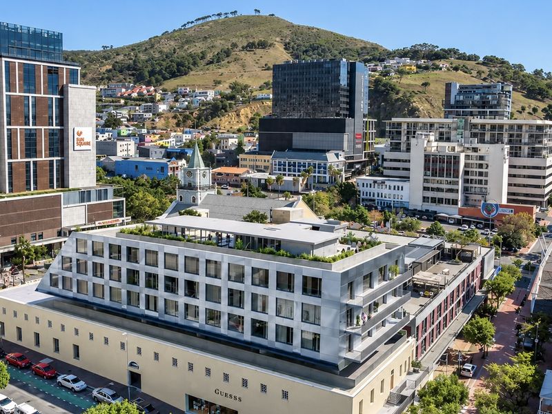 Aerial view of a modern apartment building featuring a rooftop terrace and balconies, situated in a vibrant urban neighborhood.