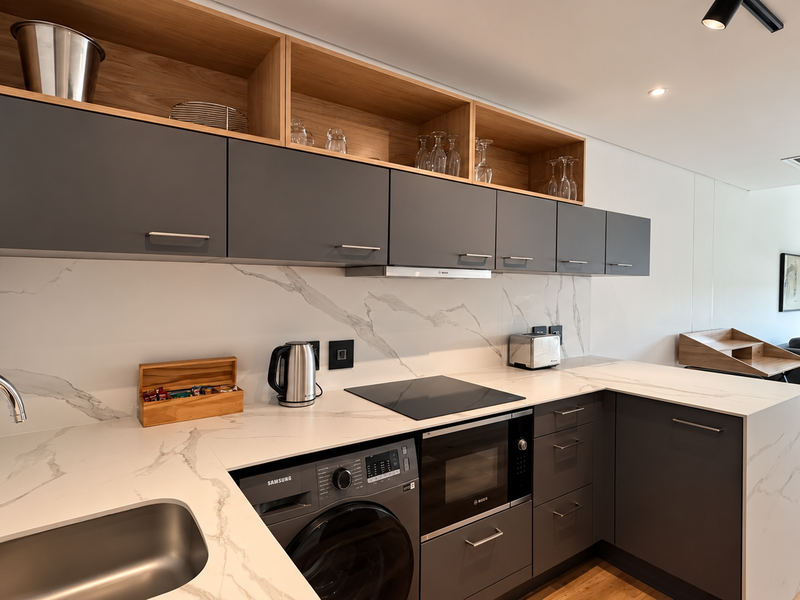 Modern open-plan kitchen featuring sleek dark cabinetry, marble-look stone surfaces, integrated appliances, and high-quality finishes, seamlessly flowing into the living area.