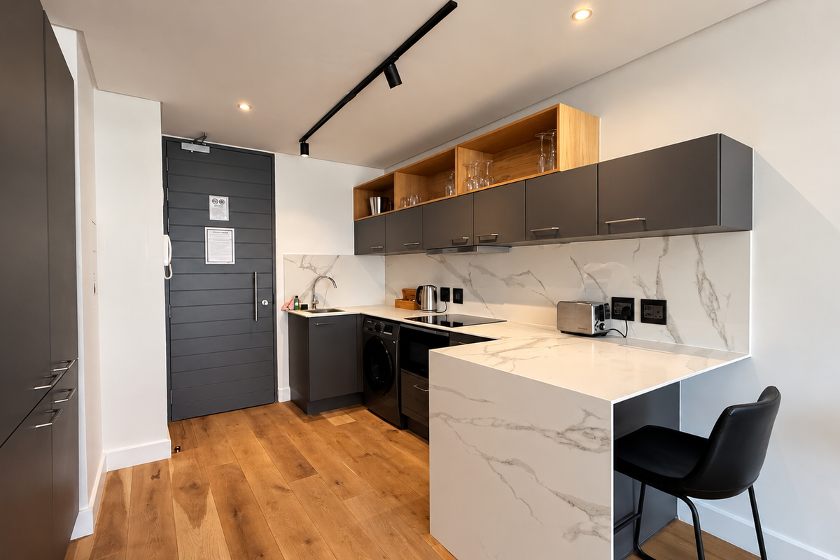 Modern kitchen featuring dark grey cabinetry, marble-look stone countertops and backsplash, integrated appliances, and timber flooring in a sleek, contemporary design.