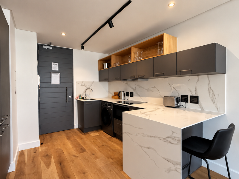 Modern kitchen featuring dark grey cabinetry, marble-look stone countertops and backsplash, integrated appliances, and timber flooring in a sleek, contemporary design.