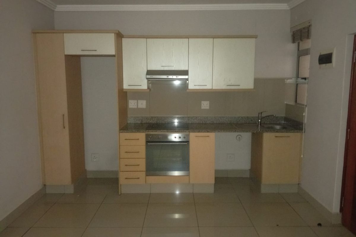 A functional kitchen featuring light wood-finish cabinetry, granite countertops, a built-in oven, hob, and extractor fan, with tiled flooring throughout.
