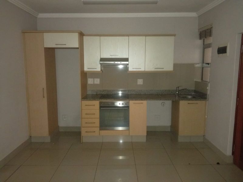 A functional kitchen featuring light wood-finish cabinetry, granite countertops, a built-in oven, hob, and extractor fan, with tiled flooring throughout.