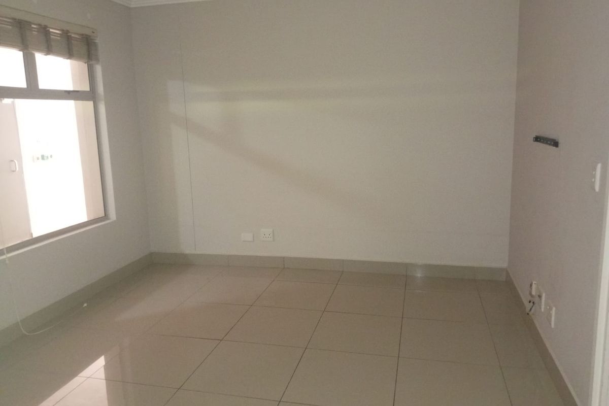 An empty bedroom featuring neutral tiled flooring, coving, and a window with a fitted roller blind.