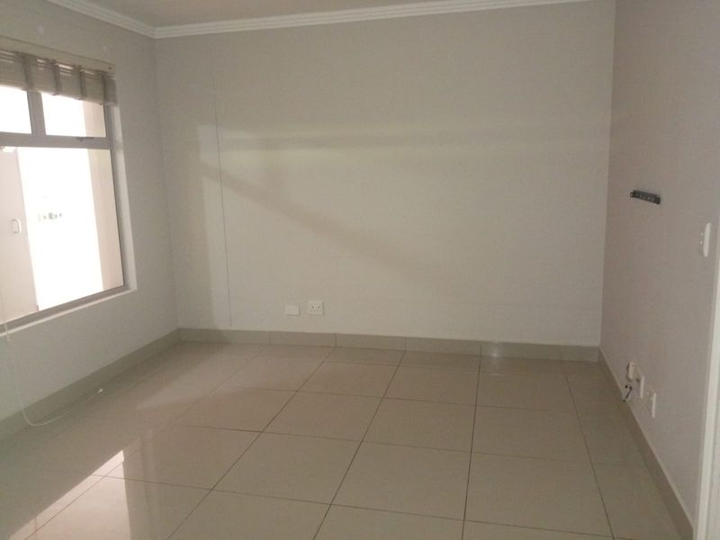 An empty bedroom featuring neutral tiled flooring, coving, and a window with a fitted roller blind.