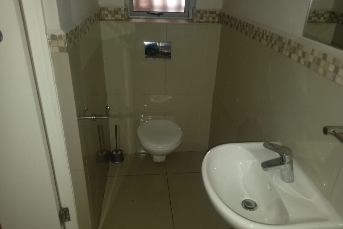 A compact guest bathroom featuring a wall-mounted toilet, a modern ceramic basin with a chrome mixer tap, and neutral tiled finishes.