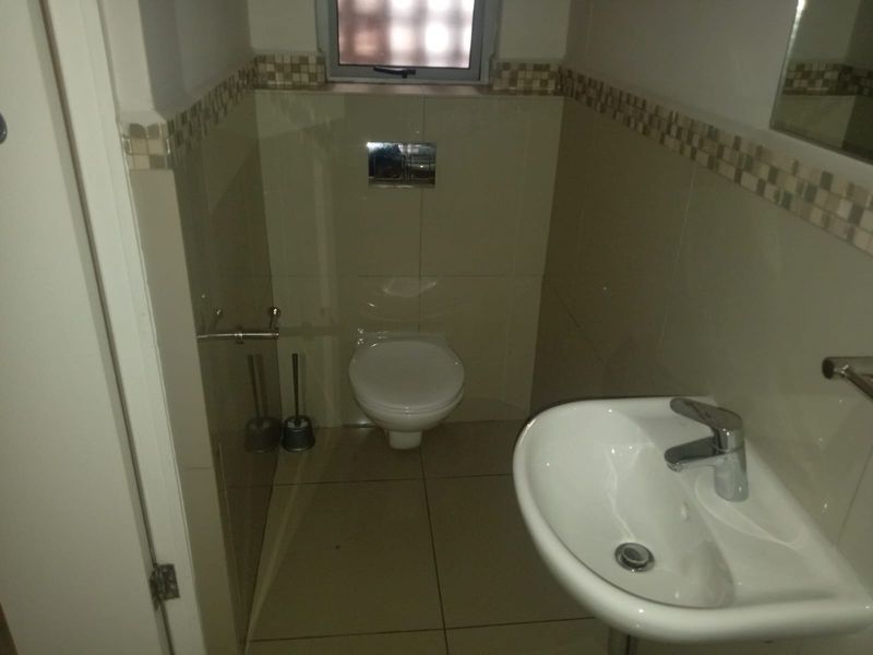 A compact guest bathroom featuring a wall-mounted toilet, a modern ceramic basin with a chrome mixer tap, and neutral tiled finishes.