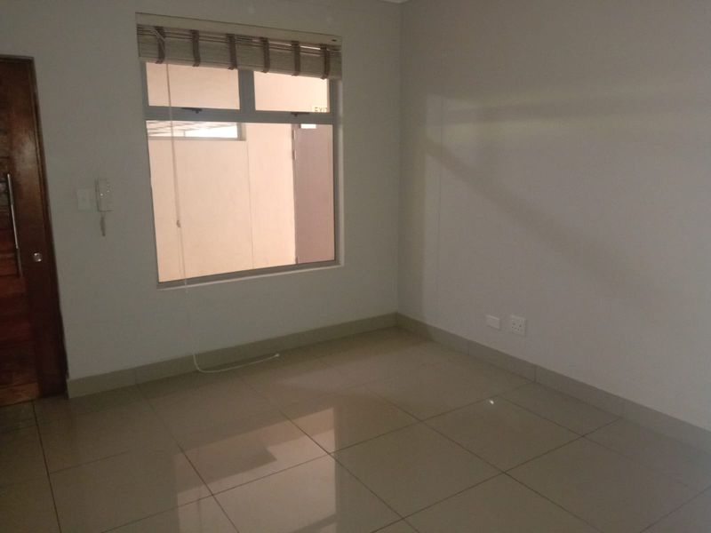 A clean, empty bedroom featuring neutral tiled flooring, an intercom system, and a window with fitted blinds, offering a blank canvas for personalization.