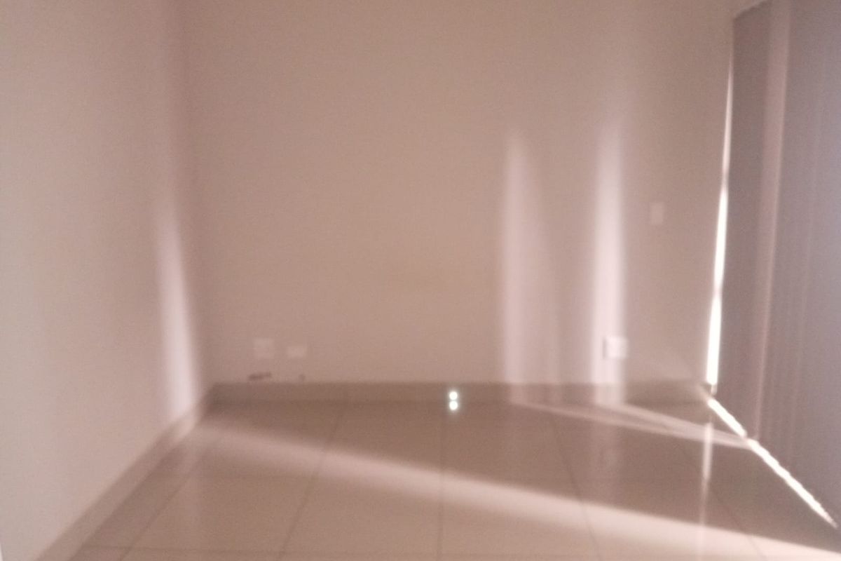 An empty, sunlit living area featuring neutral tiled flooring and vertical blinds, providing a blank canvas for interior design.