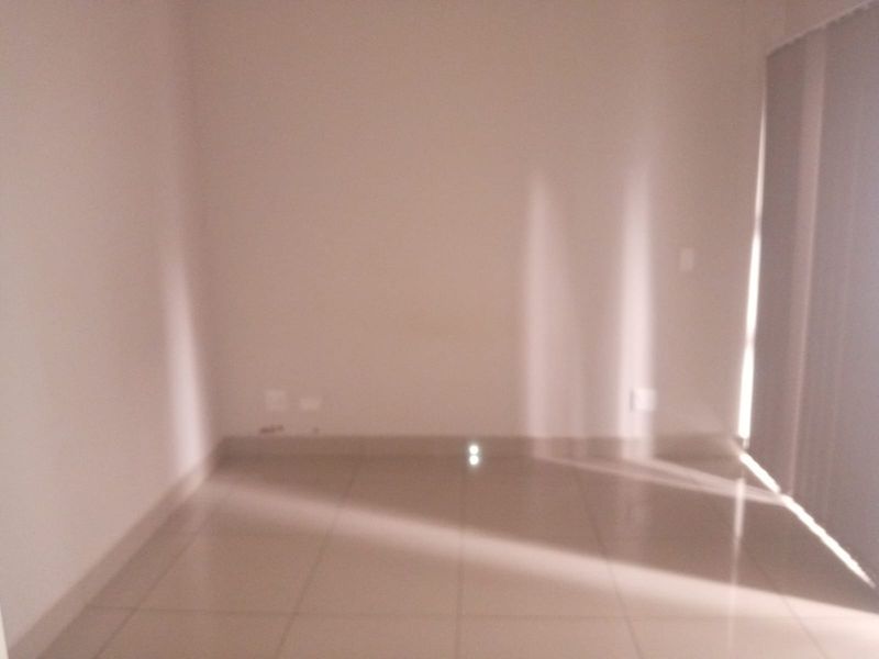 An empty, sunlit living area featuring neutral tiled flooring and vertical blinds, providing a blank canvas for interior design.