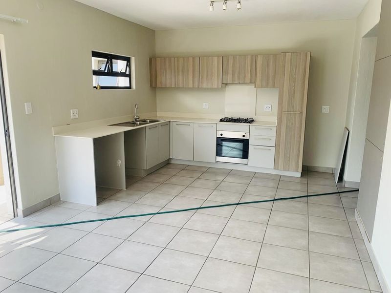 A clean, modern kitchen featuring light wood-tone cabinetry, built-in oven, gas hob, and neutral tiled flooring in an open-plan layout.