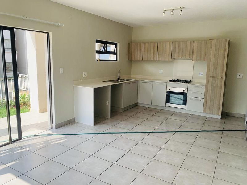 A clean, empty kitchen featuring modern built-in cabinetry, a gas hob, an oven, and tiled flooring with direct access to an outdoor patio area.