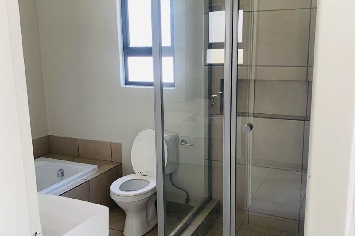 A functional bathroom featuring a separate shower enclosure, bathtub, toilet, and vanity basin with neutral tiled finishes.